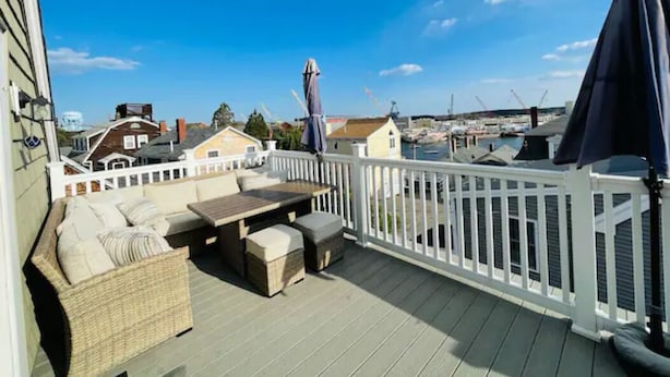 Een terras met buitenmeubilair, een witte balustrade en uitzicht op de jachthaven en gebouwen op de achtergrond.