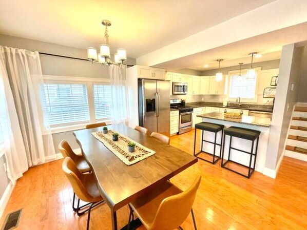 Una cocina moderna con comedor, piso de madera y una lámpara de araña.