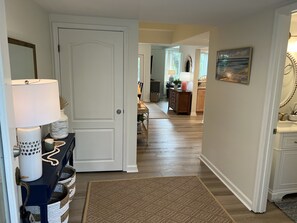 A hallway with a white door, a blue console table with a lamp, a patterned rug, and a kitchen area in the background. - Family-Friendly Townhome with Resort Amenities Included - 1/2 Mile to Beach (Edisto Beach)