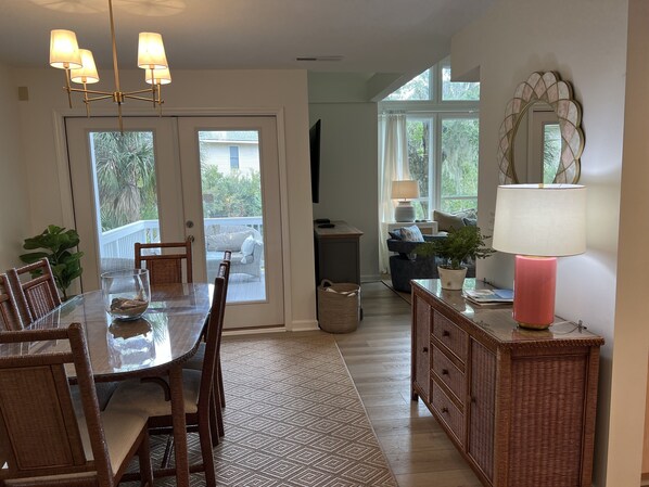 A dining area with a glass table, wicker chairs, a chandelier, and a view through the glass doors to the outside.