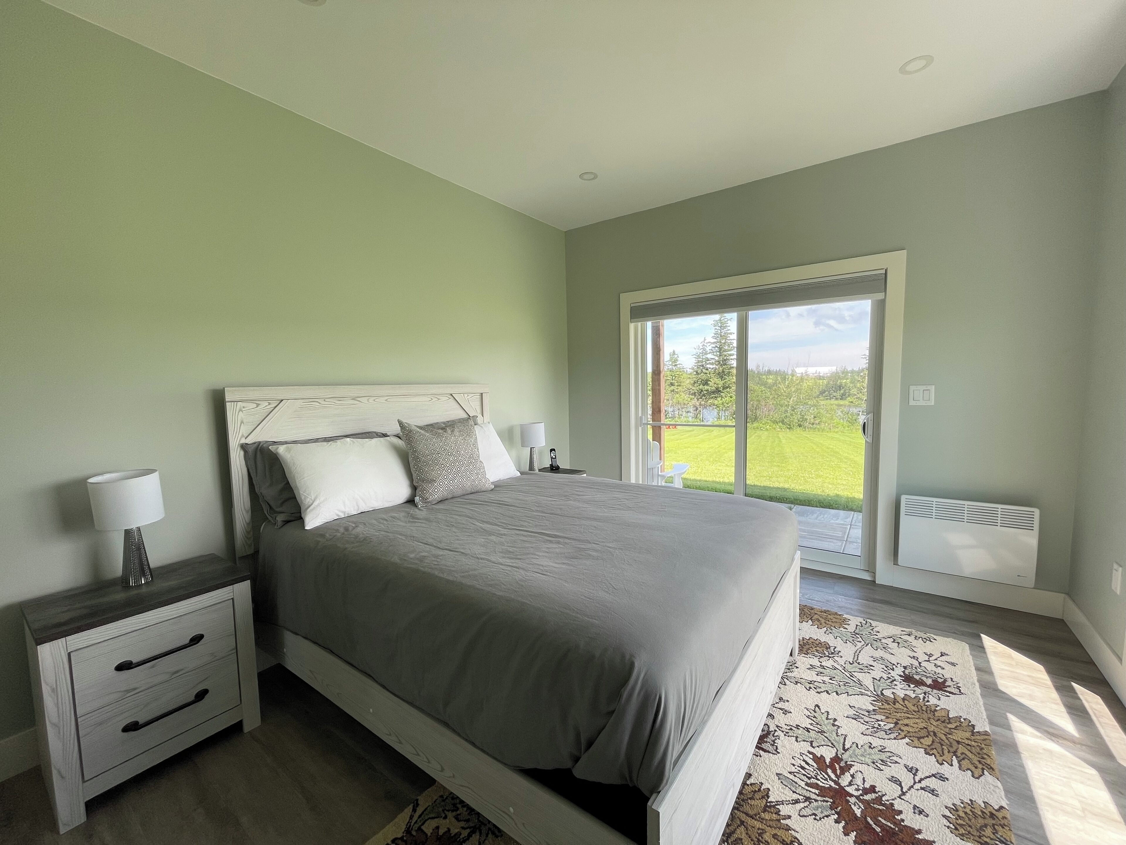 A bedroom with a bed, bedside tables, a nightstand, and a view of a green lawn through a sliding glass door.
