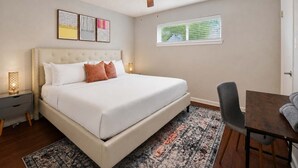 Ein Schlafzimmer mit Bett, Schreibtisch, Stuhl, Deckenventilator und Fenster mit Jalousien.
