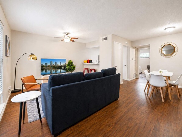 Un salon comprenant un canapé, une table à manger avec des chaises, un téléviseur, un ventilateur de plafond et une plante.