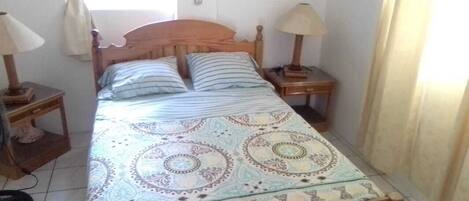 Uma cama de solteiro com colcha estampada, duas mesas de cabeceira com abajures e uma janela com cortinas.