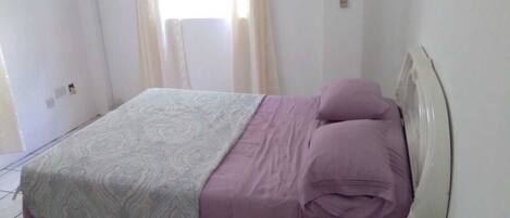 A bedroom with a bed, curtains, and a window.