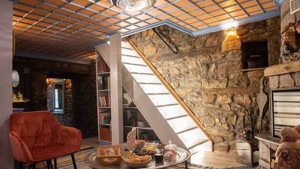 A cozy living room with a stone wall, a wooden staircase, a red chair, and a coffee table with snacks. - Dandy Villas Metsovo-Metska-Down Town-Up to 7
 (Metsovo)