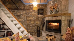 A cozy living room with a stone fireplace, a wooden staircase, and a fireplace mantel decorated with a wreath and bow. - Dandy Villas Metsovo-Metska-Down Town-Up to 7
 (Metsovo)