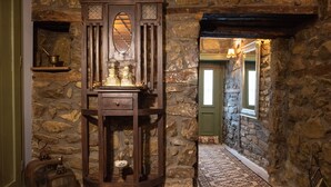 A stone-walled hallway with a wooden cabinet containing glassware, a patterned rug, and a green door at the end. - Dandy Villas Metsovo-Metska-Down Town-Up to 7
 (Metsovo)