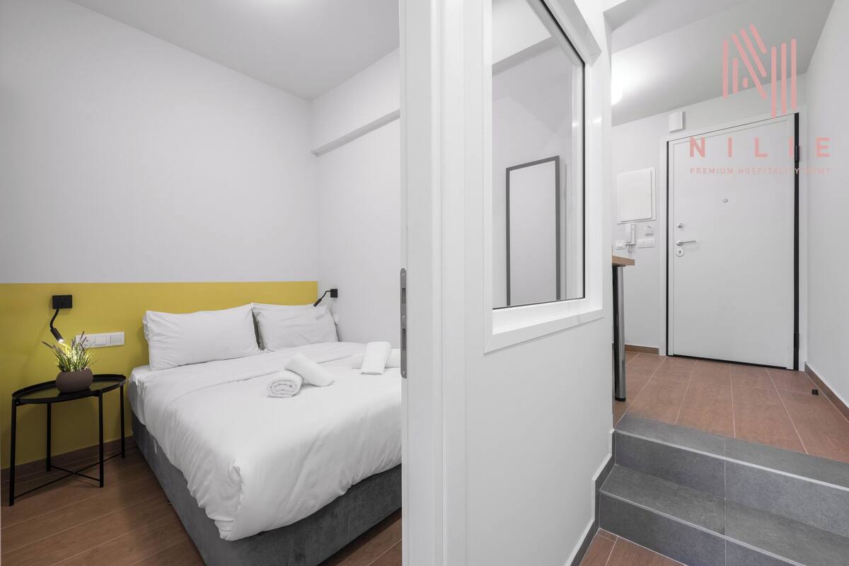 Una habitación de hotel moderna con una cama, una mesita de noche con lámpara y una pequeña planta en maceta.