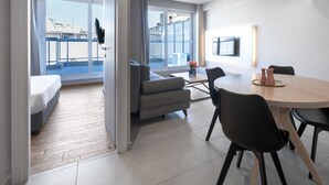 A modern hotel room with a balcony, a dining area with a round table and chairs, and a sofa.