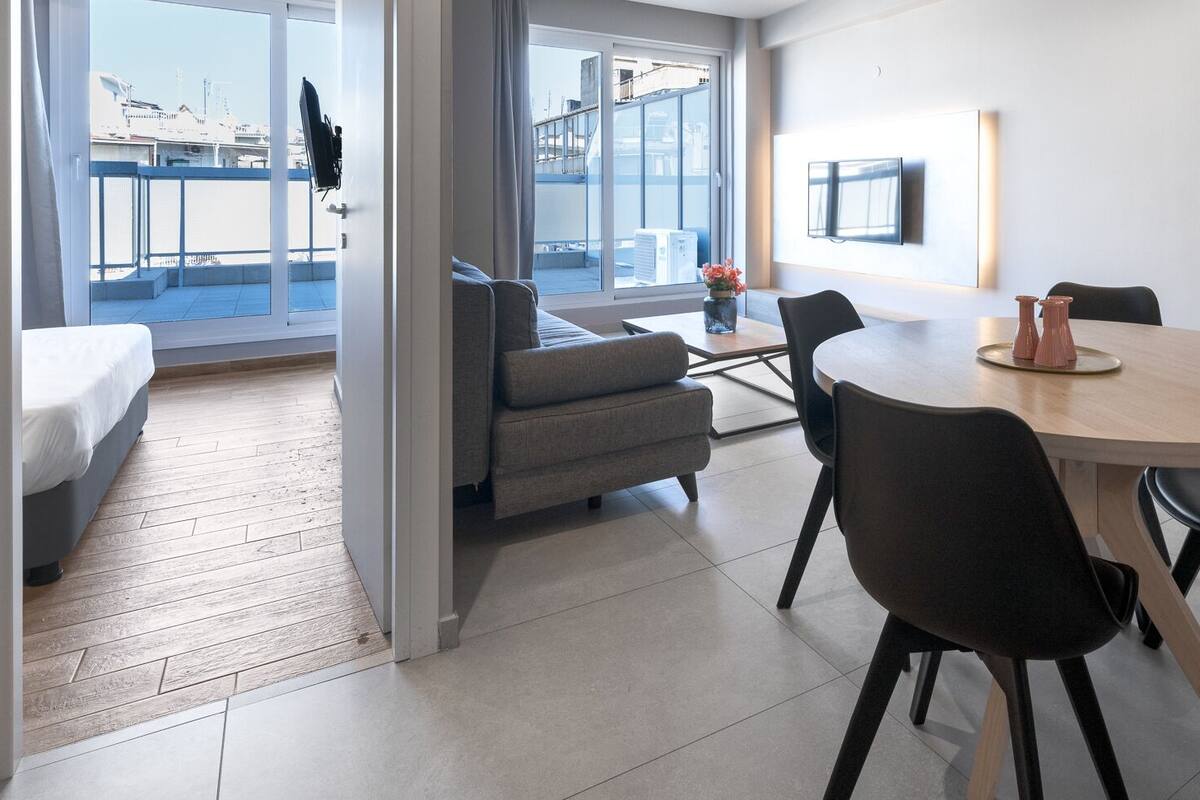 Una habitación de hotel moderna con balcón, una zona de comedor con mesa y sillas redondas, y un sofá.