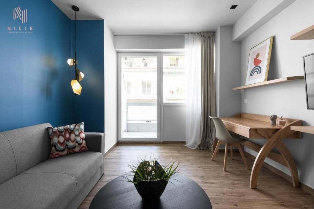 Una sala de estar moderna con una pared azul de acento, un sofá gris, un escritorio de madera y una mesa de centro negra con una planta.