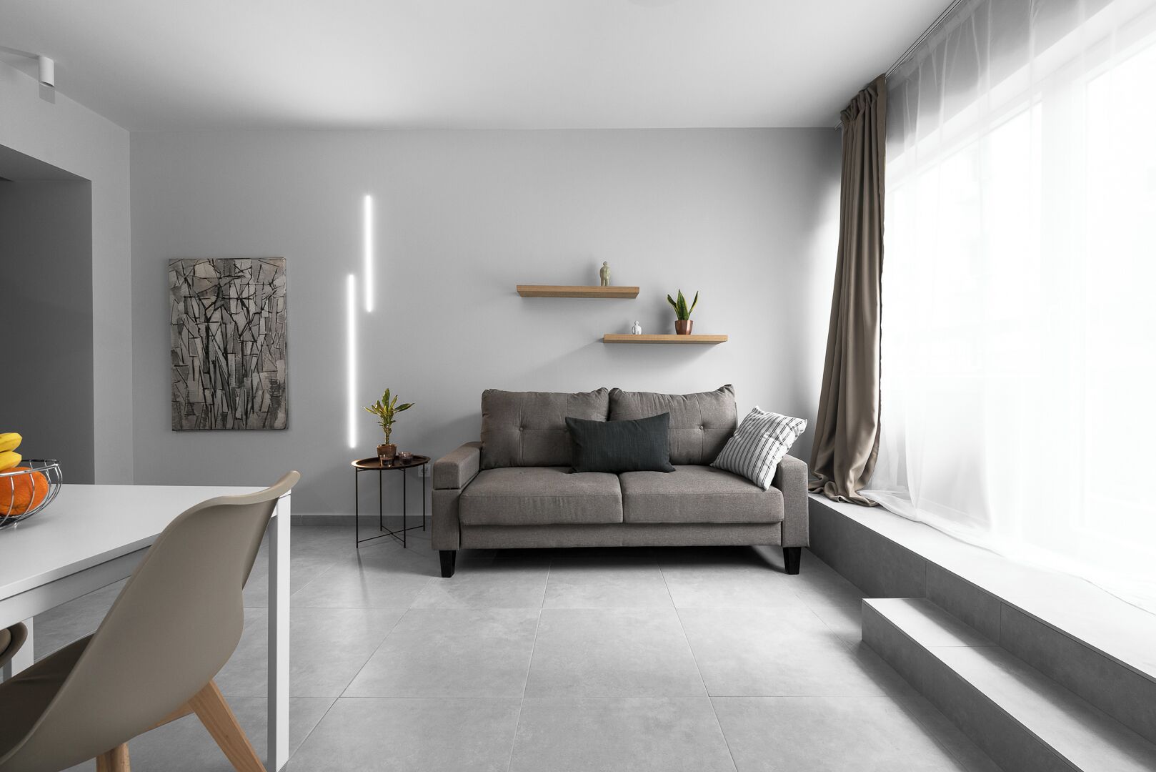 A modern living room with a grey sofa, a small side table with a plant, and a painting on the wall.