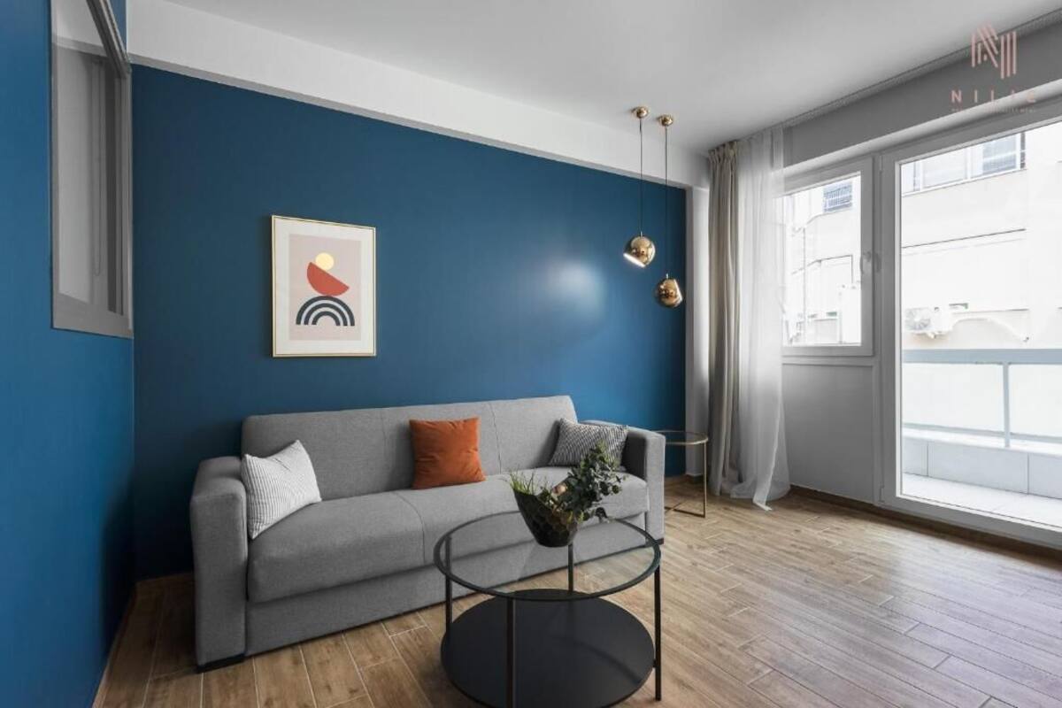Una sala de estar moderna con un sofá gris, una mesa de centro redonda y una pared azul decorativa.