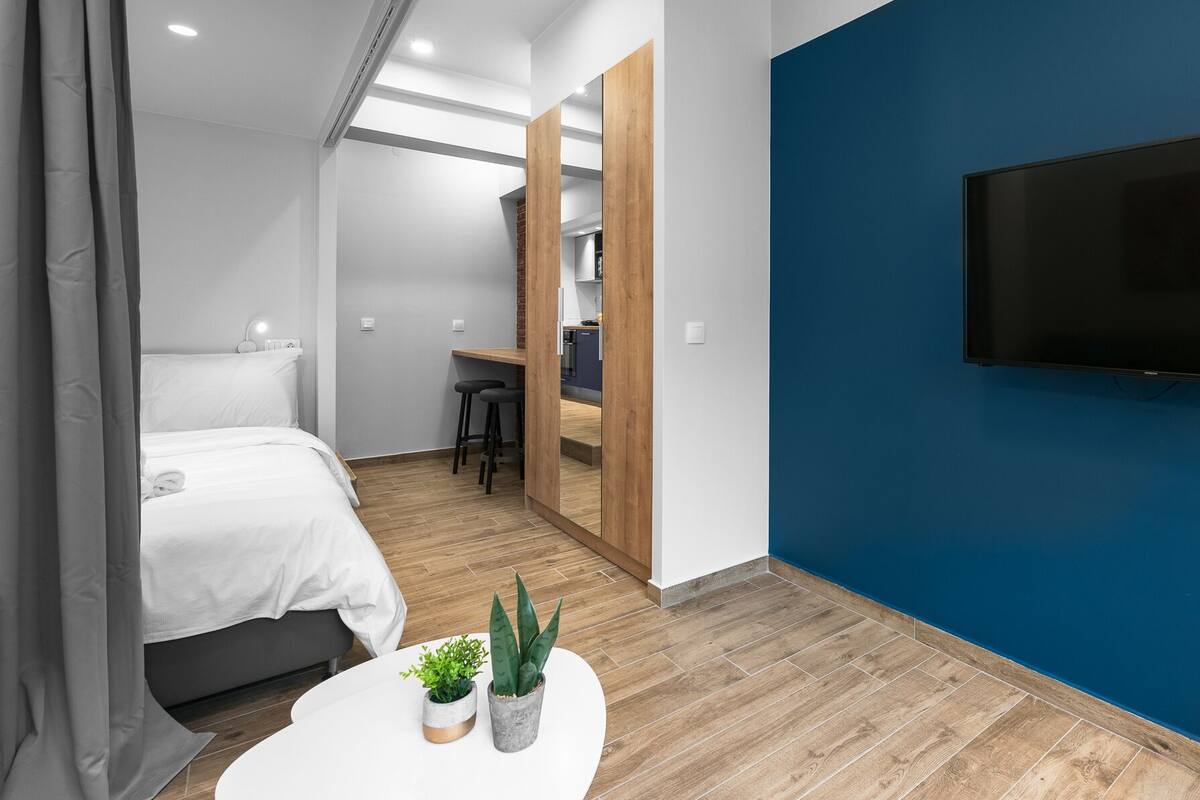 Ein modernes Hotelzimmer mit Bett, Schreibtisch, Fernseher und einem kleinen Tisch mit Pflanzen.