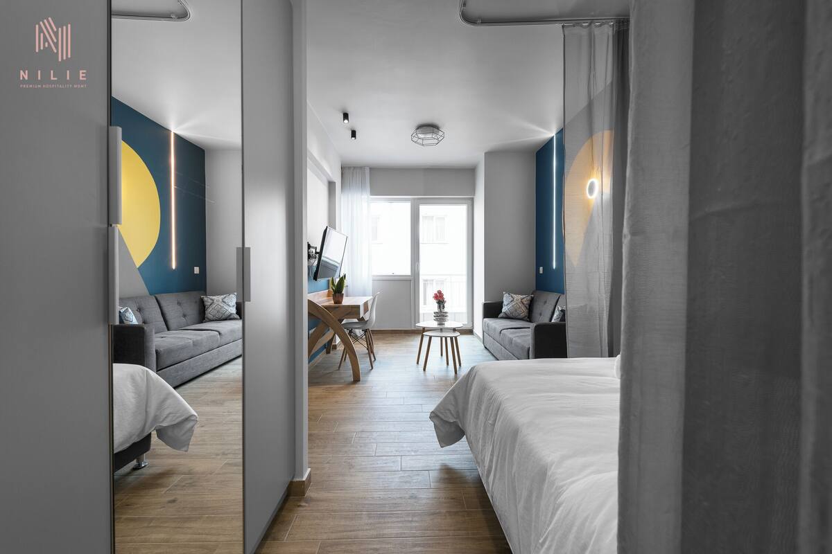 Ein modernes Hotelzimmer mit einem großen Bett, einer Sitzecke und einem Schreibtisch mit Stuhl. Ein Fenster mit Vorhängen bietet einen Blick hinaus.