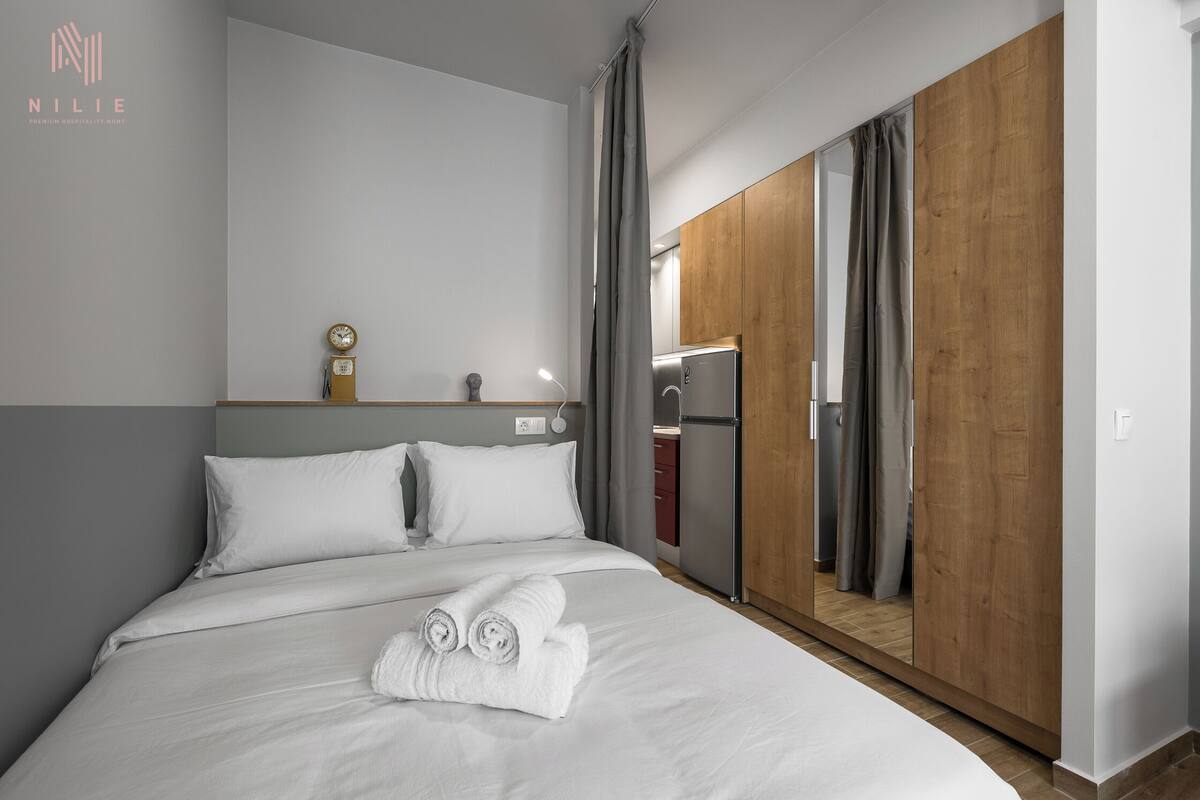 Ein modernes Hotelzimmer mit einem ordentlich bezogenen Bett, einer Nachttischuhr und einem Kleiderschrank mit Spiegel.