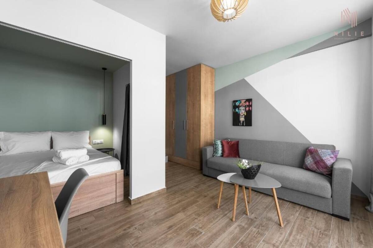 Ein modernes Hotelzimmer mit Bett, grauem Sofa, kleinem runden Tisch und einem Bild an der Wand.