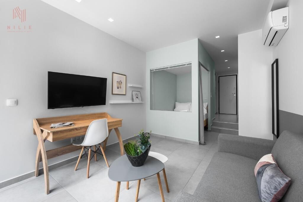 Una sala de estar moderna con un escritorio de madera, un televisor de pantalla plana, un sofá gris y una pequeña mesa redonda con una planta.