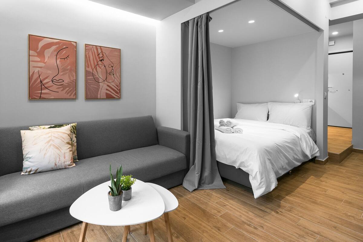 Ein modernes Schlafzimmer mit einem grauen Sofa, einem weißen Bett und zwei abstrakten Bildern an der Wand.