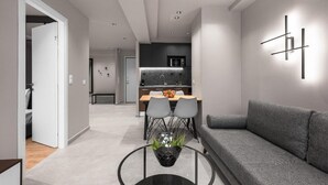 A modern living room with a grey sofa, a dining area with a table and chairs, and a kitchen in the background.