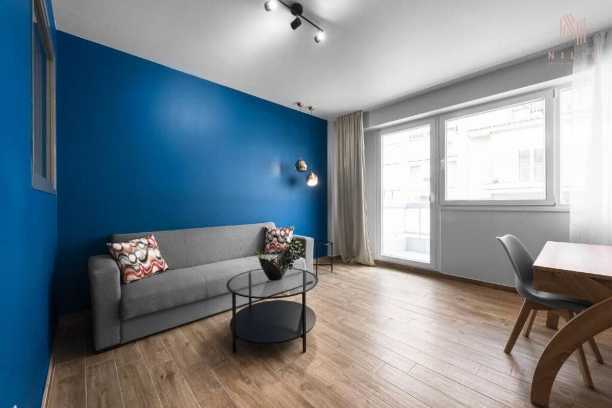 Una sala de estar moderna con una pared azul de acento, un sofá gris, una mesa de centro redonda y un comedor con mesa y sillas de madera.