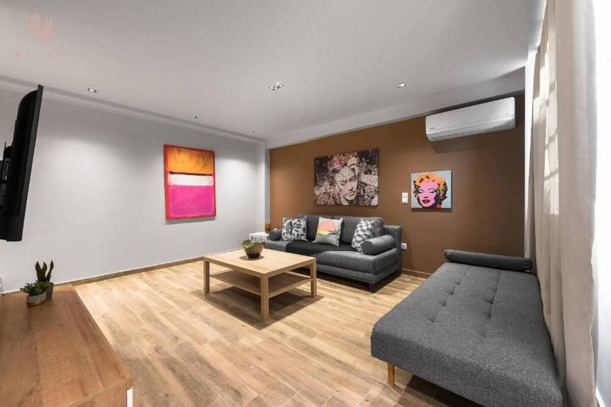 Una sala de estar moderna con un sofá gris, una mesa de centro de madera y un sofá gris. Hay dos cuadros en la pared y una planta en maceta en el suelo.
