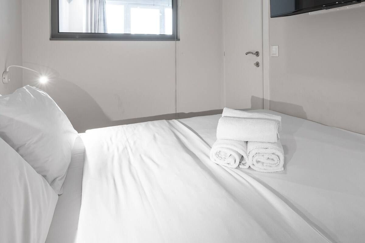 Una habitación de hotel con cama, mesita de noche, ventana y puerta.