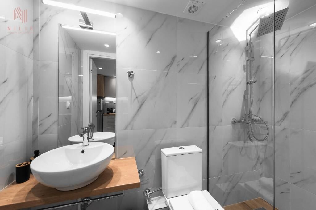 A modern bathroom with a large marble sink, a glass shower enclosure, and a visible toilet.