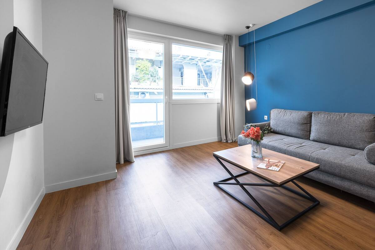Una sala de estar moderna con un sofá gris, una mesa de centro de madera y un televisor montado en la pared.