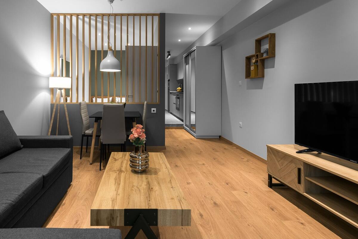 Una sala moderna con un sofá, un mueble para TV y una zona de comedor con mesa y sillas.