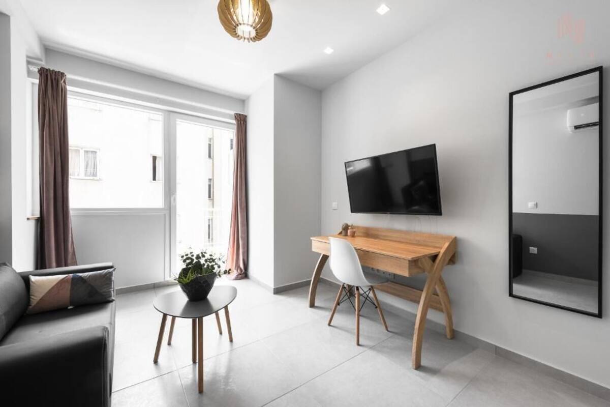 Ein modernes Wohnzimmer mit einer Couch, einem Holztisch, einem Fernseher und einem großen Fenster mit Vorhängen.