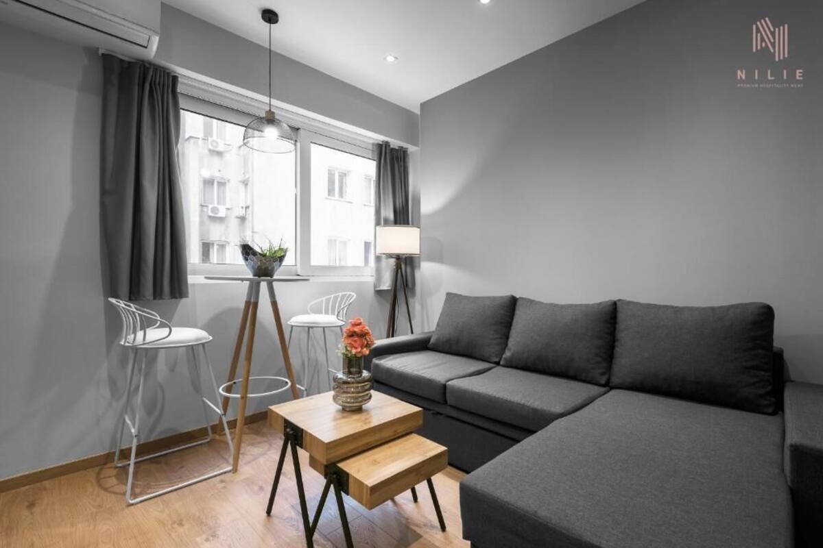 Ein modernes Wohnzimmer mit einem grauen Sofa, einem Holztisch und einem kleinen Beistelltisch mit einer Blumenvase.