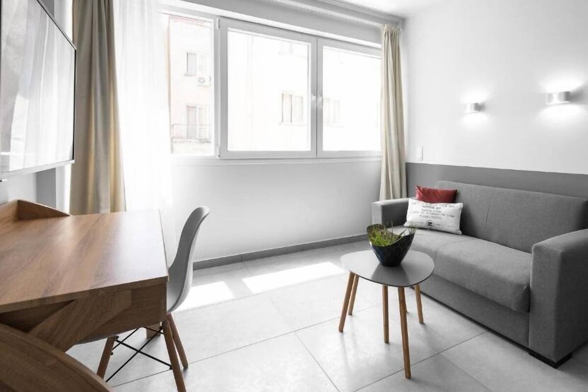 Ein modernes Wohnzimmer mit einem grauen Sofa, einem kleinen runden Tisch mit einer Pflanze, einem Holzesstisch und einem Stuhl.