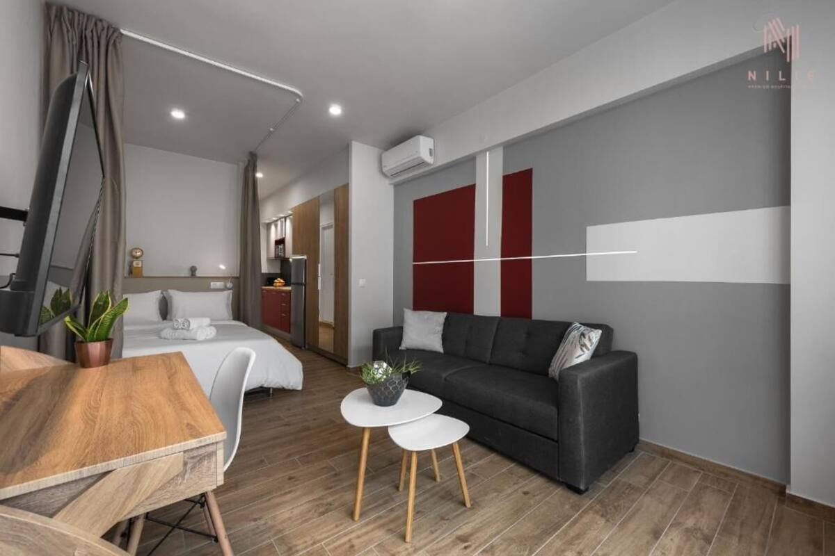 Ein modernes Hotelzimmer mit einem Holztisch, einem grauen Sofa, einem kleinen weißen Couchtisch und einem Bett mit weißen Leinen.
