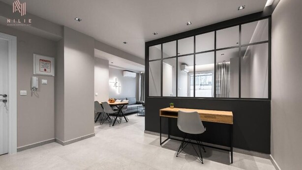 A modern hotel room with a large window, a desk, and a dining area.