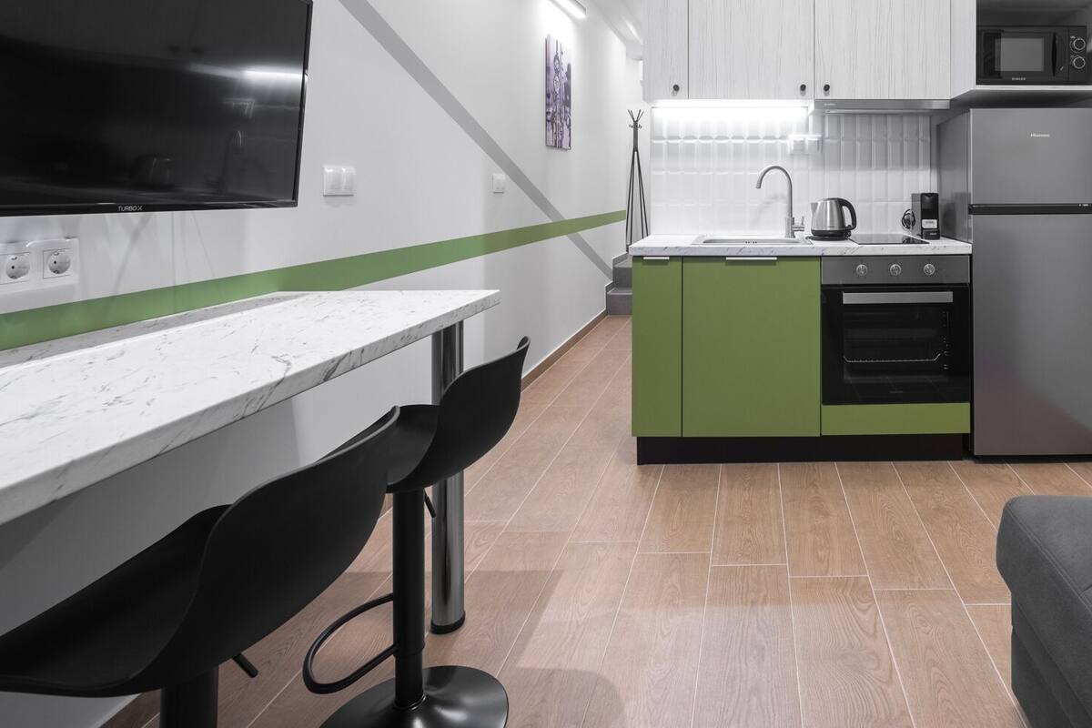 Una cocina compacta con comedor, un sofá y un televisor colocado en la pared.