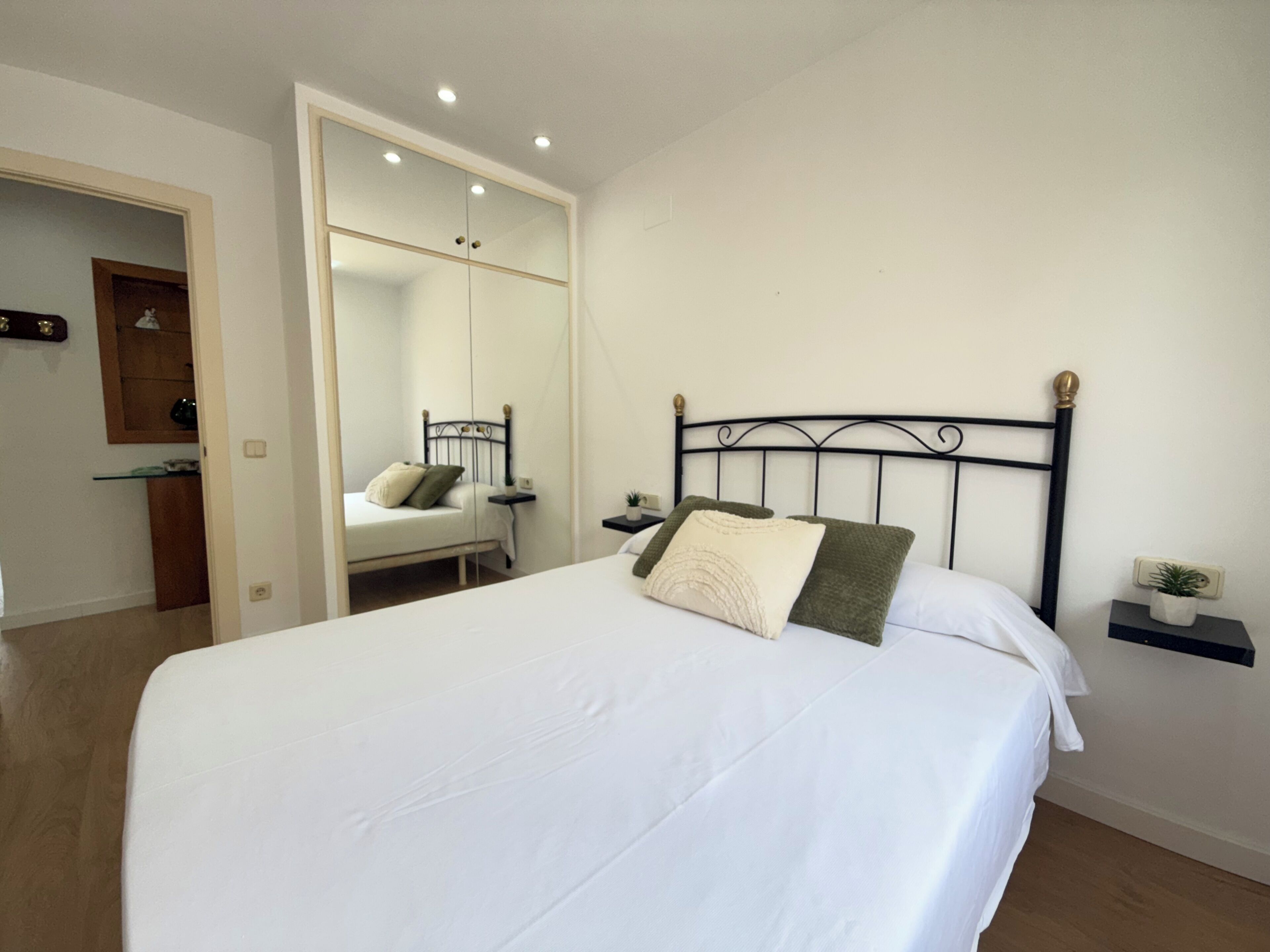 Un dormitorio con cama, mesita de noche, espejo y una pequeña estantería.
