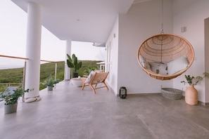 A modern outdoor patio with a hanging chair, a cushioned chair, and potted plants.