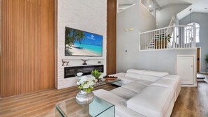 Un salon moderne avec un canapé blanc, une table basse en verre, une cheminée et un grand téléviseur fixé au mur.