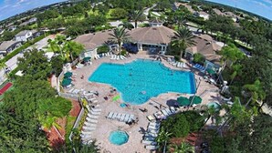 Vue aérienne d’un complexe hôtelier doté d’une grande piscine, entourée de chaises longues et de palmiers.
