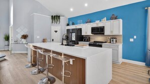 Une cuisine moderne avec des meubles blancs, un îlot central doté de tabourets et un mur d’accent bleu.