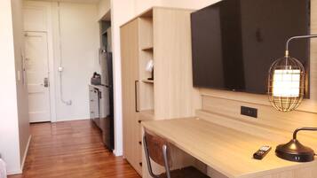 Una habitación de hotel moderna con un escritorio de madera, una silla, un televisor de pantalla plana, una lámpara y un control remoto.