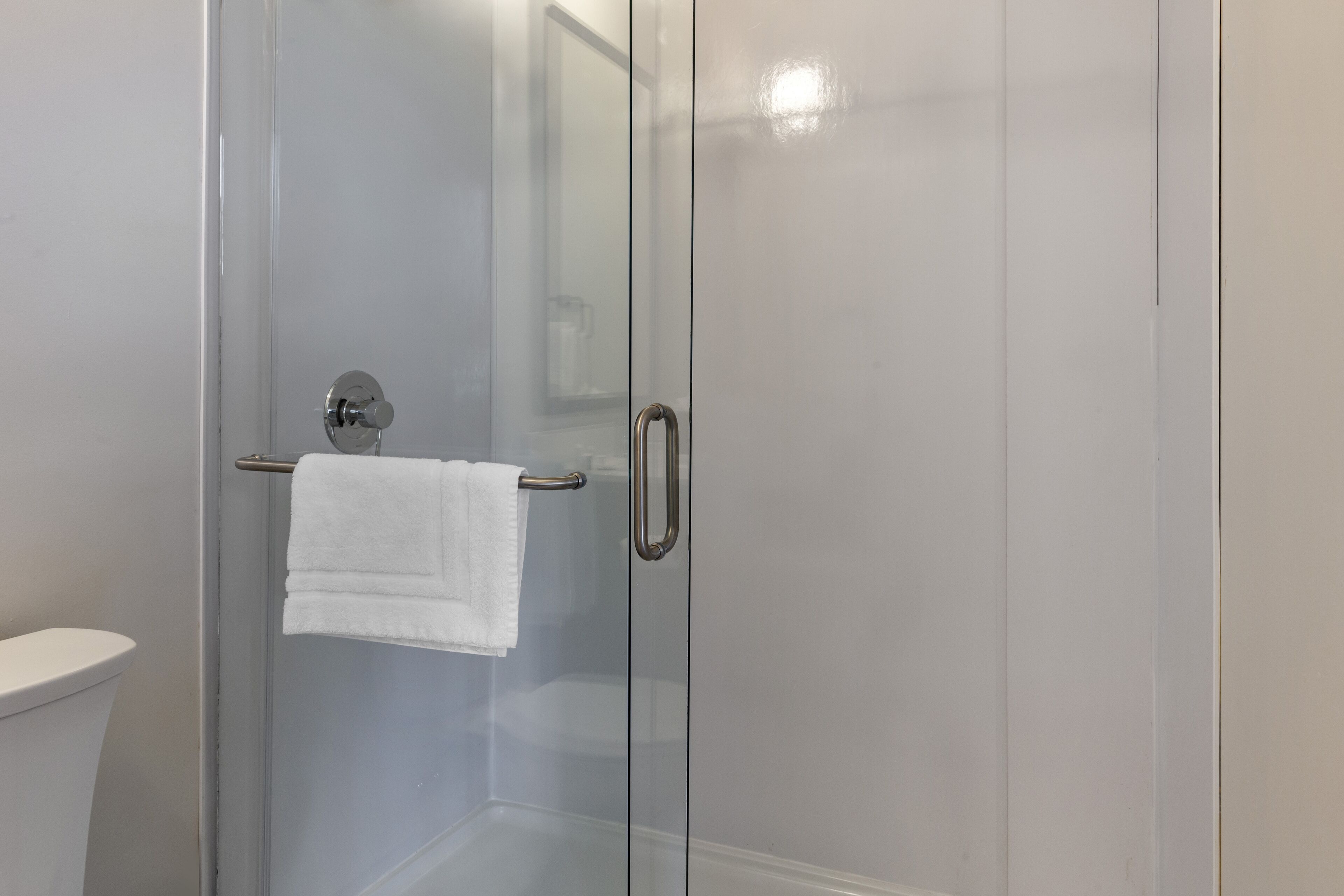 A glass-enclosed shower with a white towel on a metal bar.