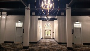 Un couloir d’hôtel avec un lustre, des portes blanches et une moquette à motifs.