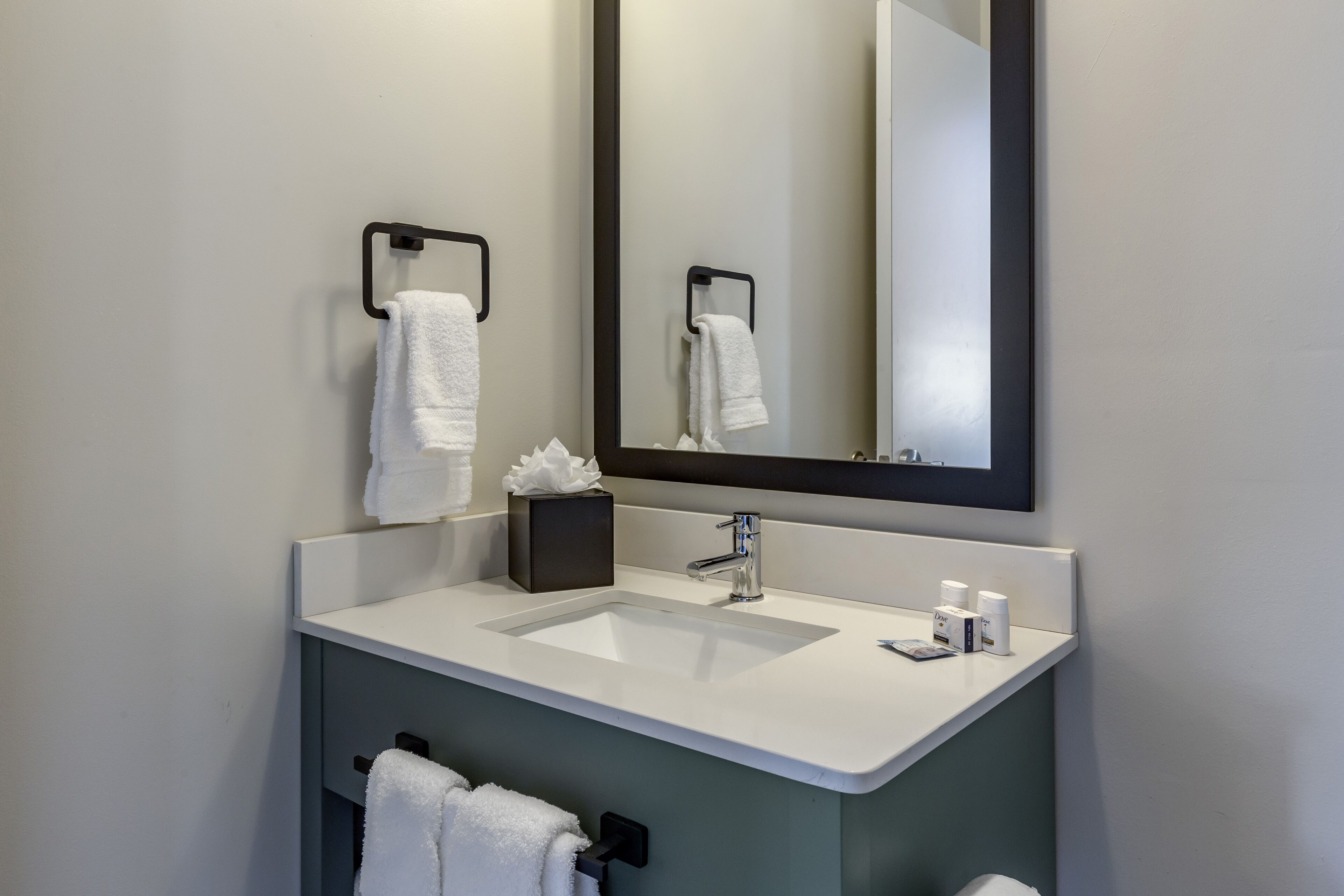 Un baño moderno con un lavabo blanco, un espejo grande y dos toalleros.