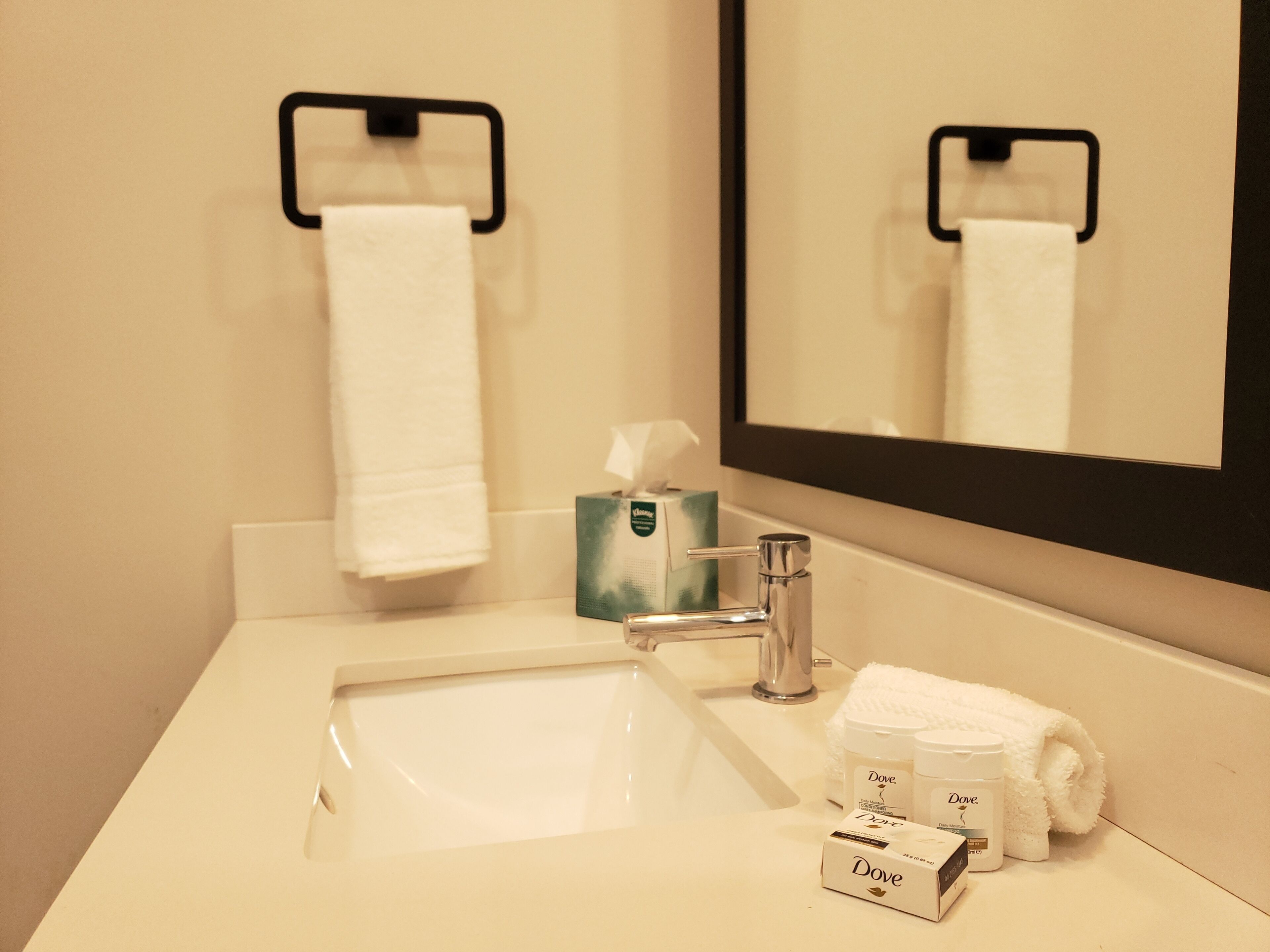 A bathroom with a white sink, a mirror, a towel rack, and Dove toiletries.