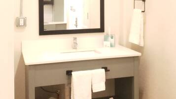 A bathroom with a white sink, a mirror, a towel rack, and a shelf with towels.