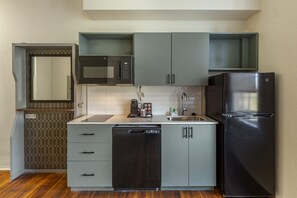 A compact kitchen with a dishwasher, a black refrigerator, a microwave, and a coffee maker.