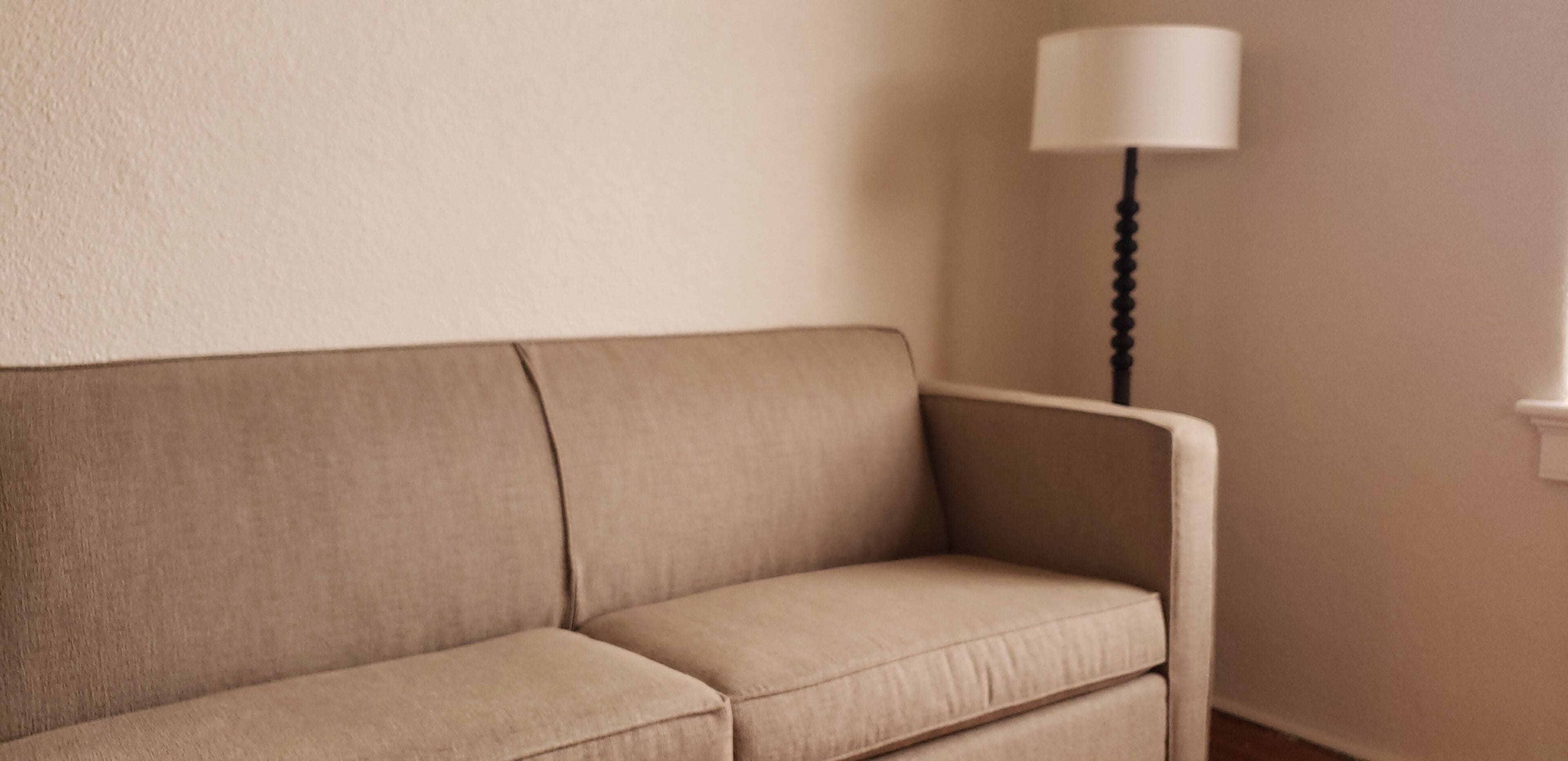 Un canapé beige dans une pièce dont le mur est uni et qui est éclairée par un lampadaire.